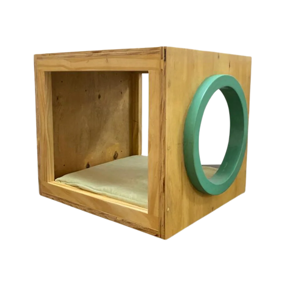 Caja de madera hueca empotrable en su color natural, es la Cama Kira para gatos, tiene un cojín cama en el interior y una entrada circular color verde en la parte frontal de la caja