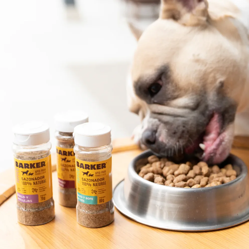 Un perro pug comiendo sus croquetas con 3 frascos del Sazonador Pollo y Mollejas a su lado